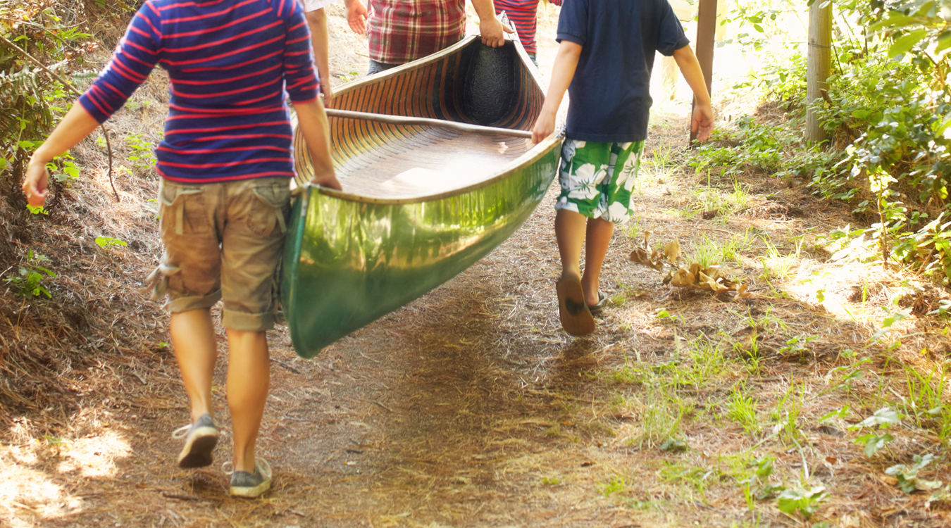View of a family carrying a canoe down a path towards the water.